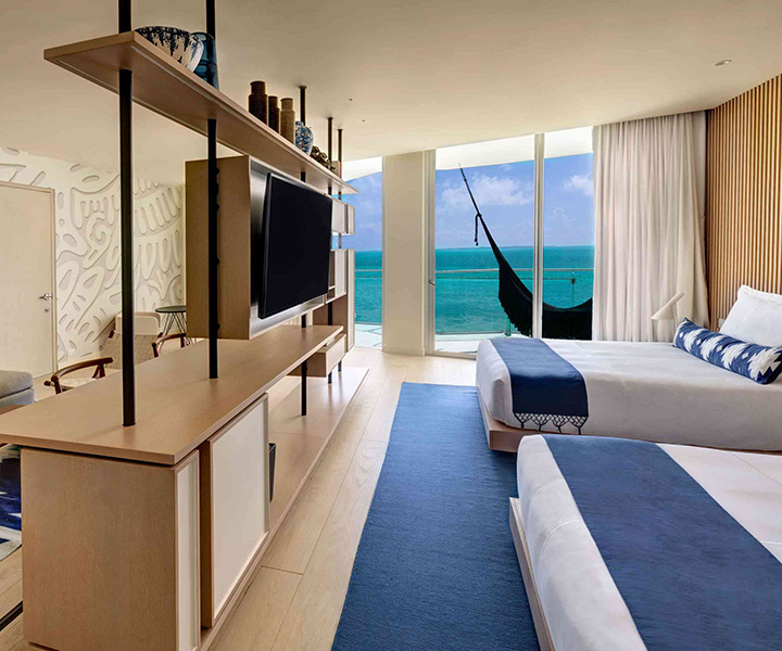 Luxurious hotel room with two beds and a sleek television, offering ultimate comfort and entertainment and a balcony with a hammock overlooking the ocean.
