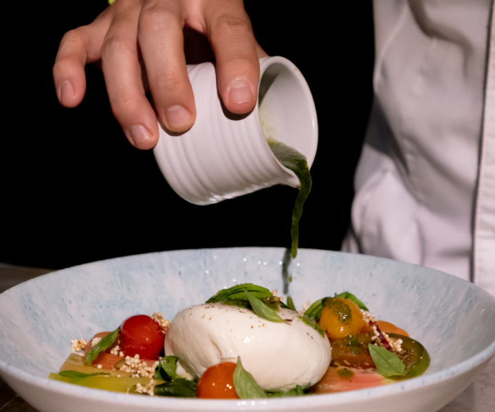 a chef pouring balsamic on a burrata and tomato salad