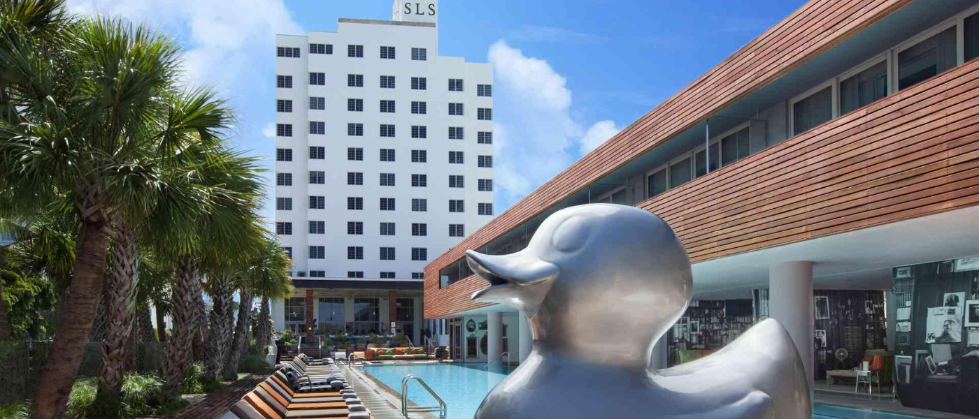 uma escultura gigante de um pato prateado em frente a uma piscina