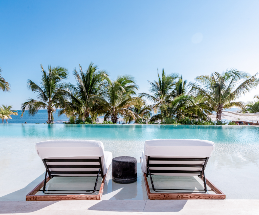 two daybeds in front of a pool with palm trees in the distance