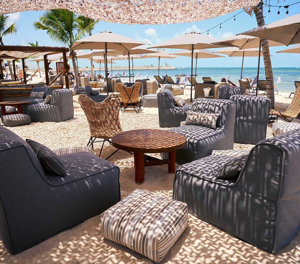 Cenário de praia luxuoso com cadeiras elegantes e chapéus-de-sol cheios de estilo na areia dourada.