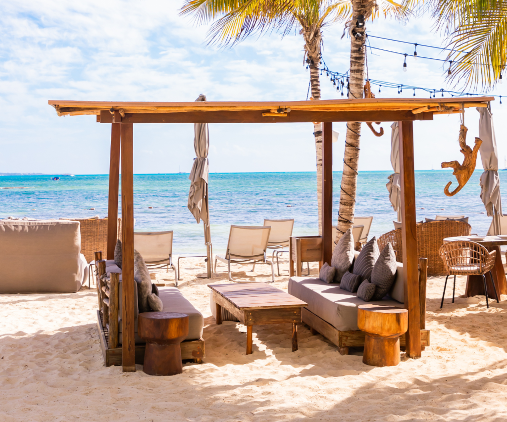 a wooden cabana with plush seating on the beach