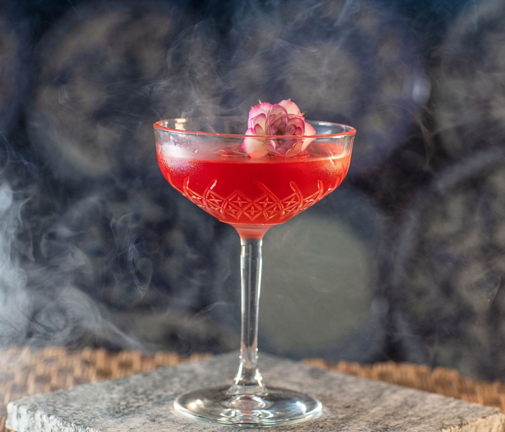 Red cocktail in a etched crystal coupe glass, topped with a flower