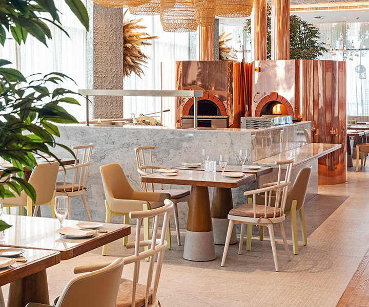 Interior of Fi'lia dubai restaurant, set with modern tables and chairs and two rose gold pizza ovens.