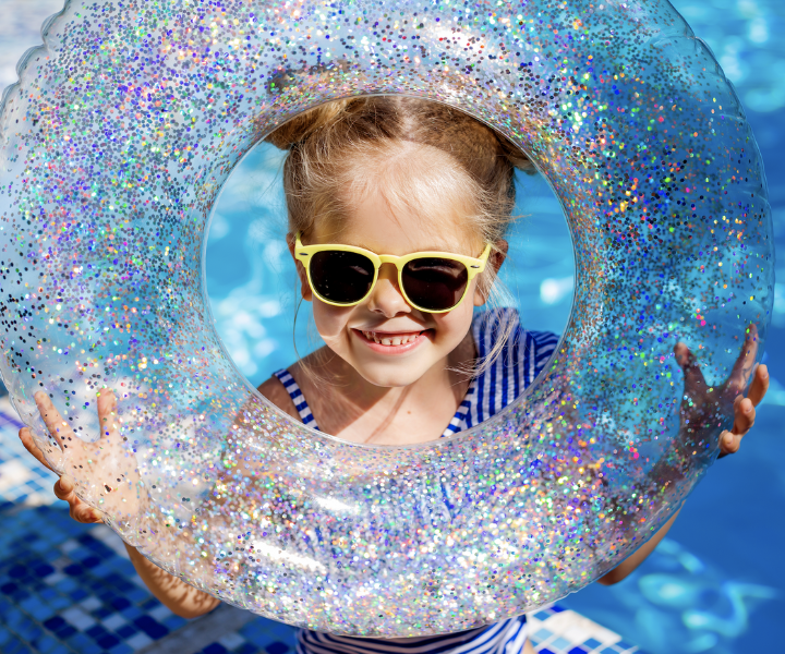 a smiling kid wearing sunglasses with a pool floatie