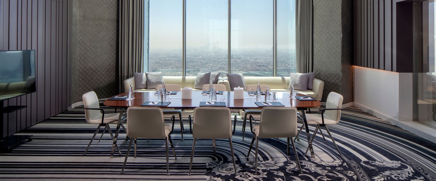 Large meeting room with a long table and white chairs, a TV and floor to ceiling windows with city views. 