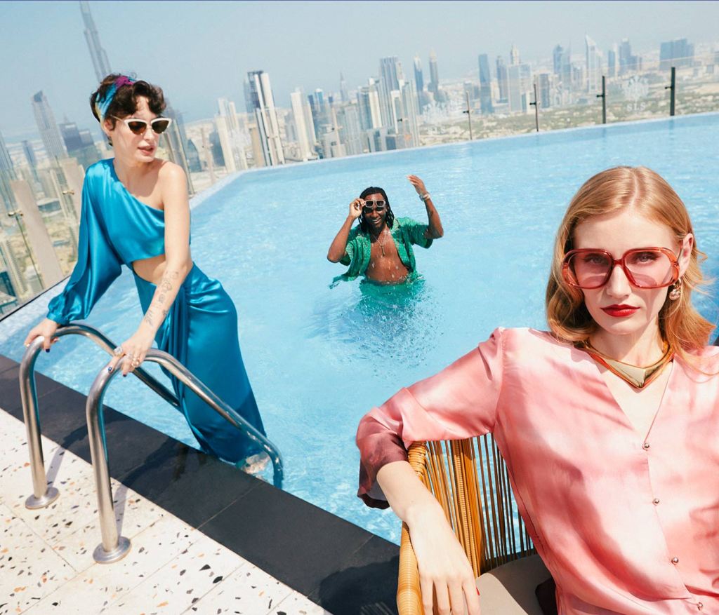 Two people in a rooftop pool and one person in a chair in the foreground