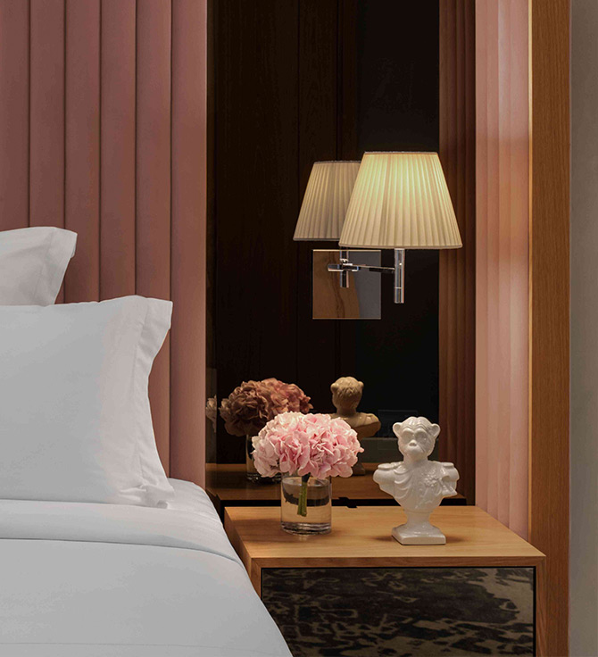 Chambre luxueuse avec élégant drap blanc sur le lit et superbe table de nuit sur laquelle est posée une lampe chic.