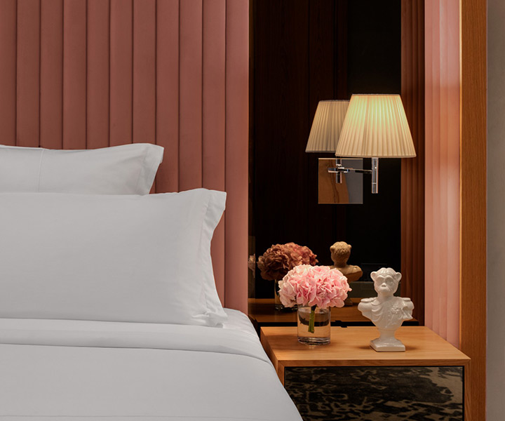 Luxurious bedroom with pristine white sheets on a cozy bed, elegantly accompanied by a stylish lamp.