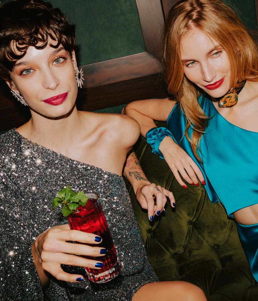 one woman in a sparkly silver dress holding a red cocktail next to a woman in a silky blue dress