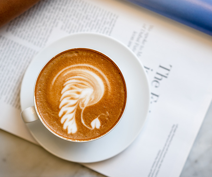 Close-up with a latte with a design on top of it, placed on top of a page of a magazine.