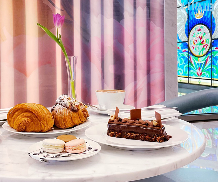 Una mesa en EllaMia en SLS Dubai con pasteles y café colocada frente a una hermosa vidriera.