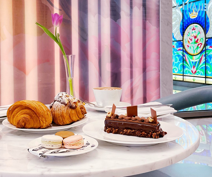 Une table à EllaMia au SLS Dubaï avec des pâtisseries et du café posée devant un magnifique vitrail.