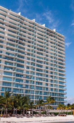 White and glass building, exterior of SLS Cancun, overlooking the beach with a colorful, oversized duck statue.