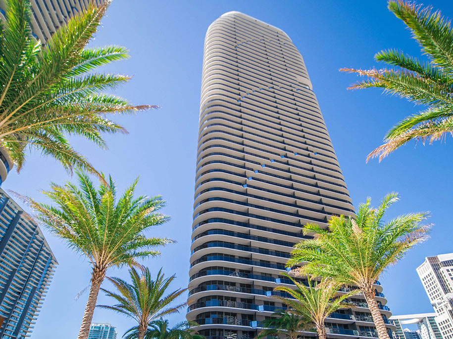 Modern white and glass skyscraper exterior of SLS LUX Brickell hotel with palm trees on the street.