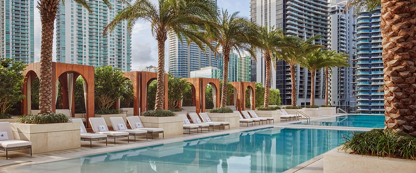 The pool on the 9th floor terrace of SLS LUX Brickell in Miami, lined with palm trees and cabanas