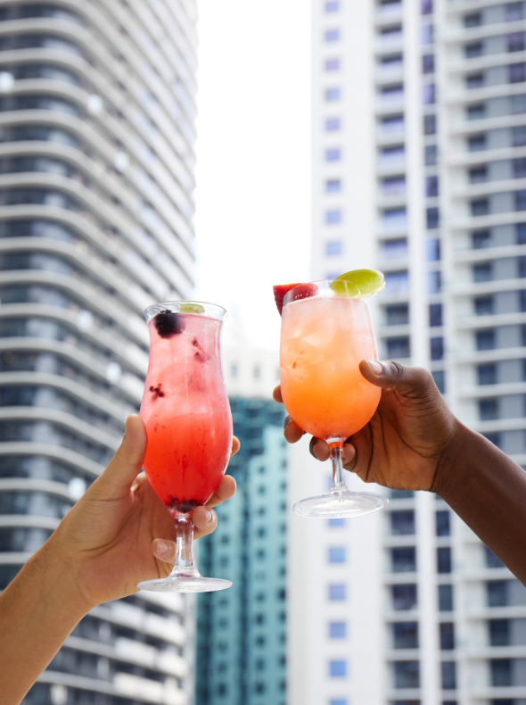 Two cocktails being raised in front of the downtown Miami skyline
