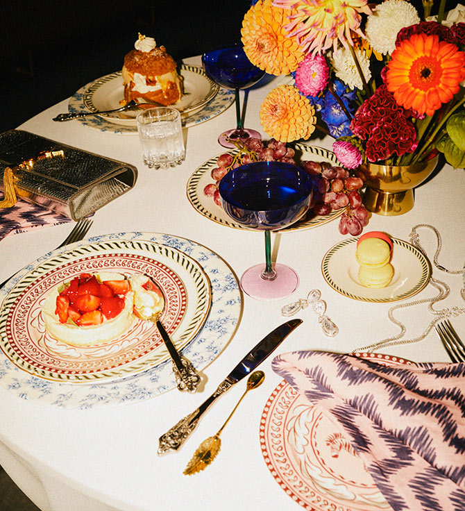 A lavish dining setting with ornate plates, a dessert, macarons and blue cocktail.