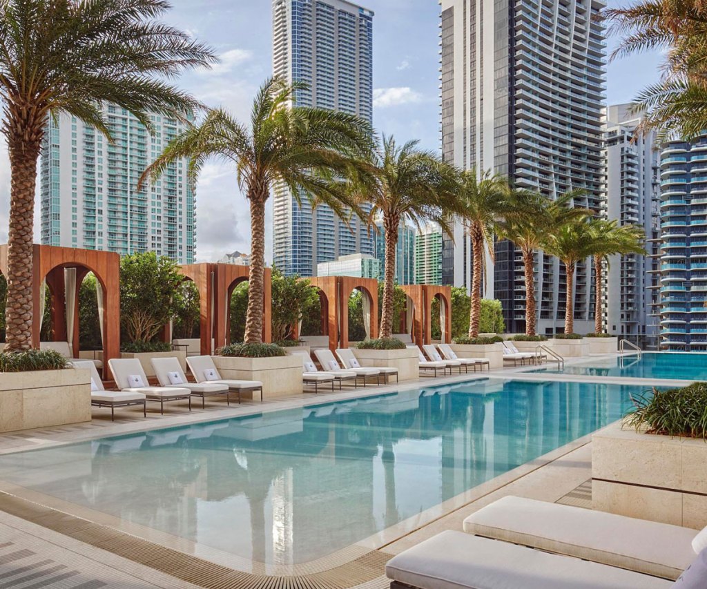 Rooftop pool lined with daybeds, cabanas and palm trees.