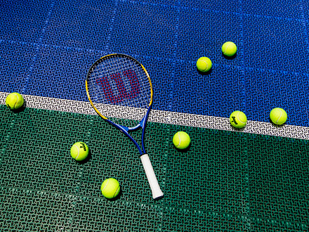 Tennis racquet with tennis balls laying on a tennis court.