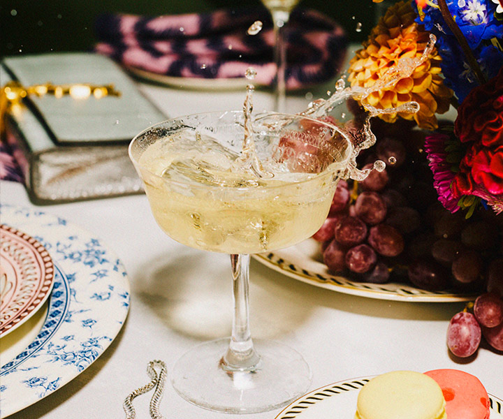 Éclaboussures d'un magnifique verre à cocktail sur une table richement décorée de fleurs et de macarons.