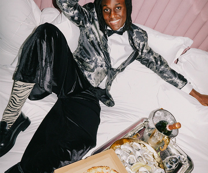 A stylish man in a suit and tie sitting on a luxurious bed.