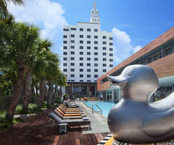 uma escultura gigante de um pato prateado em frente a uma piscina