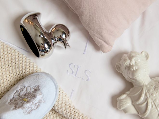 A silver duck, slipper, monkey bust and pink pillow on a SLS branded bed.