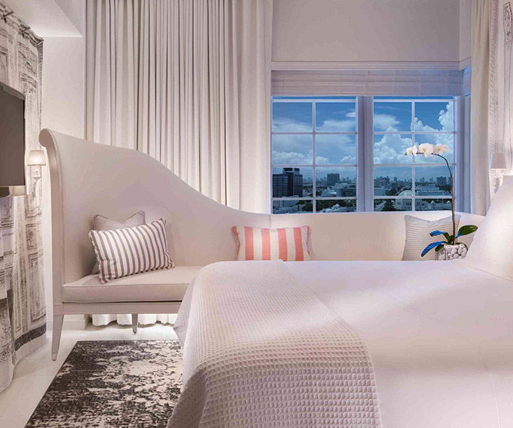 Lujosa habitación de hotel con una distinguida cama, un elegante sofá y un gran ventanal que ofrece unas vistas impresionantes.