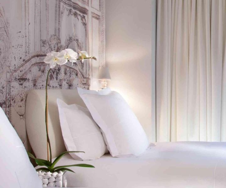 Luxurious white bed adorned with plush white pillows and a vase of fresh flowers.