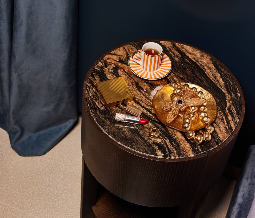 A bedside table with a white and orange striped espresso cup and saucer and red lipstick