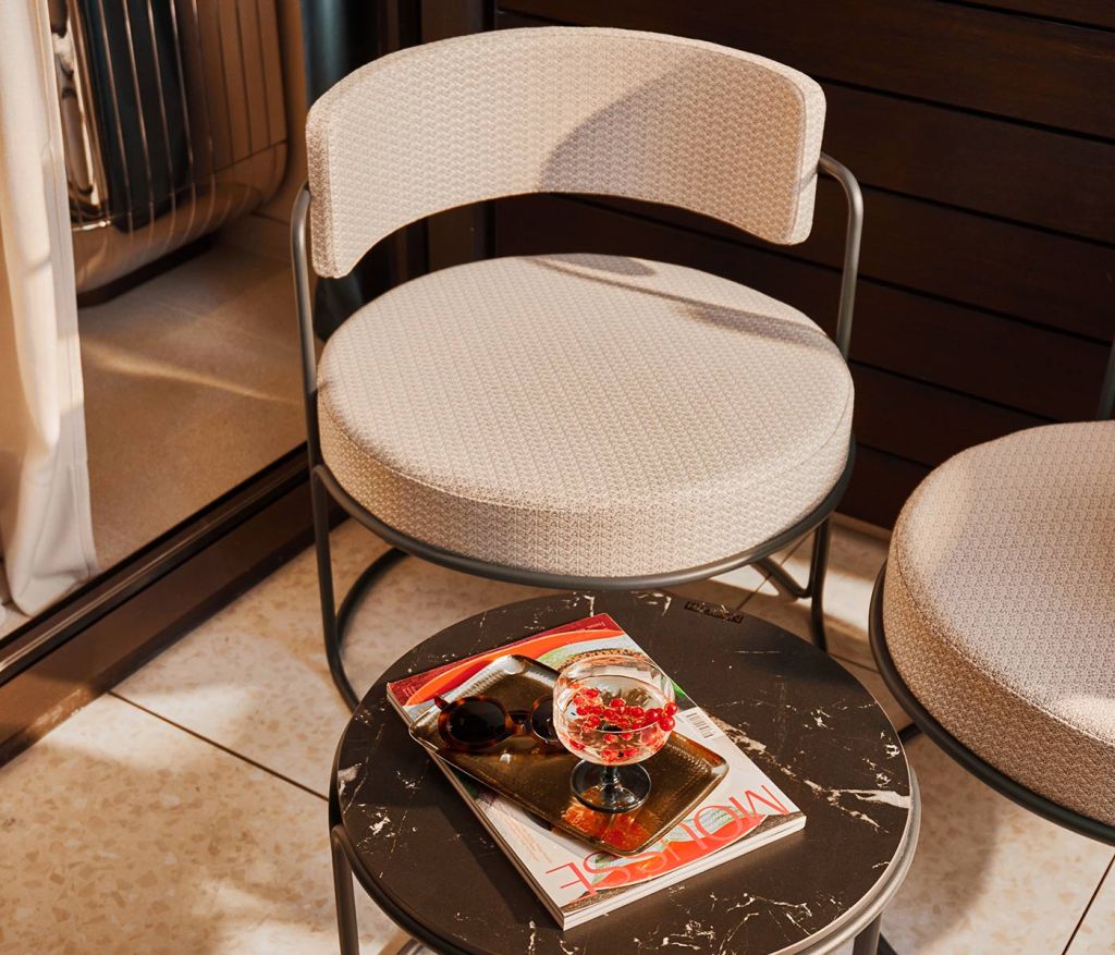 Rounded chair on a balcony in front of a small table with reading material and a drink