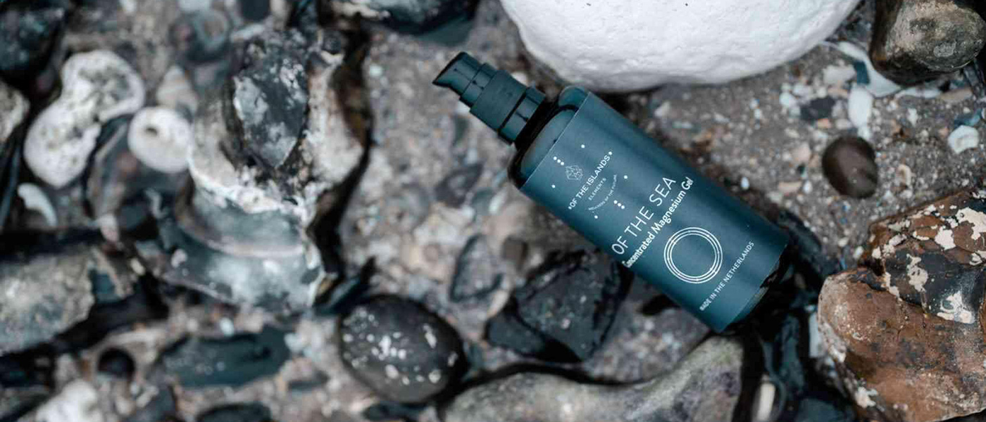 Of the Sea spa product in a dark blue bottle laying on rocks