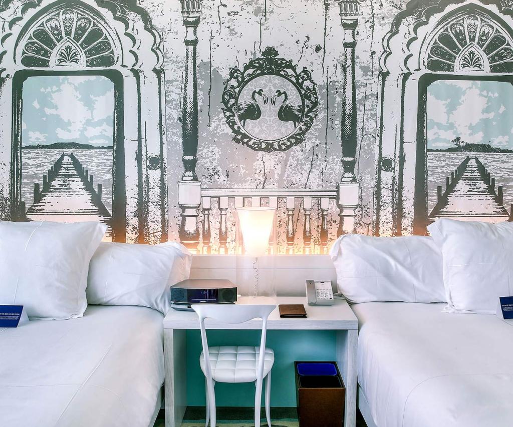 Dos elegantes camas en una habitación lujosamente decorada, con un cautivador mural de adorno.