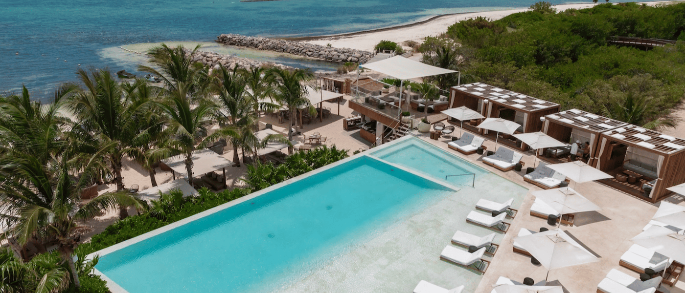 an aerial shot of a beautiful pool surrounded by palm trees with luxurious white lounge chairs surrounding it.