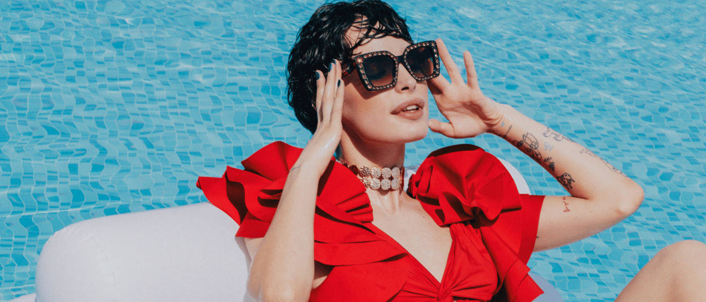 a woman on a white floatie in the pool wearing a red swimsuite and luxurious sunglasses