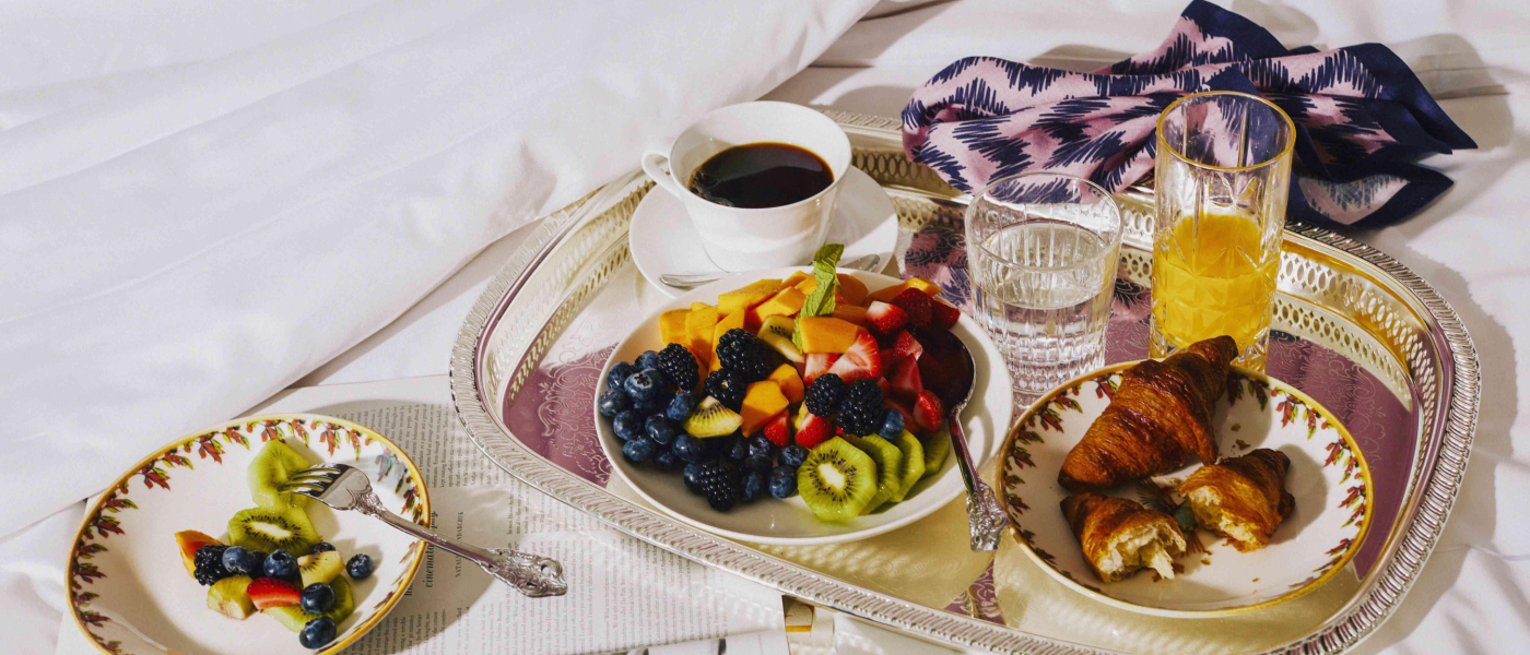 A luxurious scene with a coffee cup, delicious breakfast, and a magazine elegantly placed on a plush bed, creating a cozy and sophisticated ambiance.