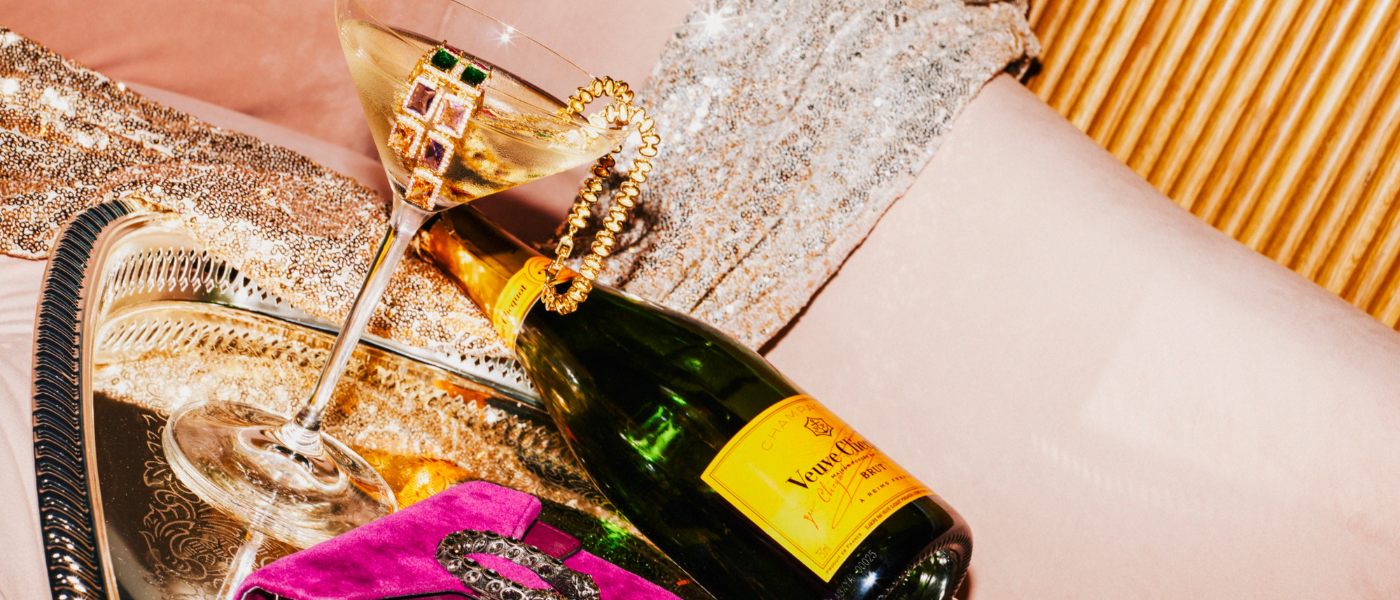 a bottle of veuve on a silver platter next to a champagne glass draped with gold