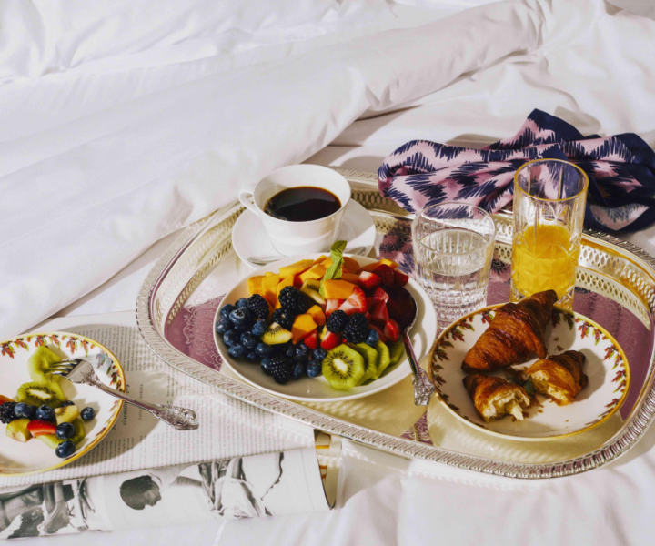 Une scène luxueuse avec une tasse de café, un délicieux petit-déjeuner et un magazine élégamment placé sur un lit moelleux, créant une ambiance chaleureuse et sophistiquée.