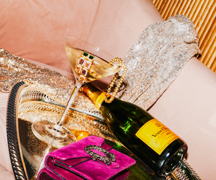 a bottle of veuve on a silver platter next to a champagne glass draped with gold