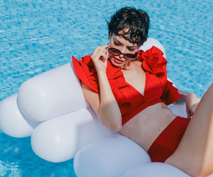 a woman sitting in a pool on a floatie wearing a stylish red swimsuit 