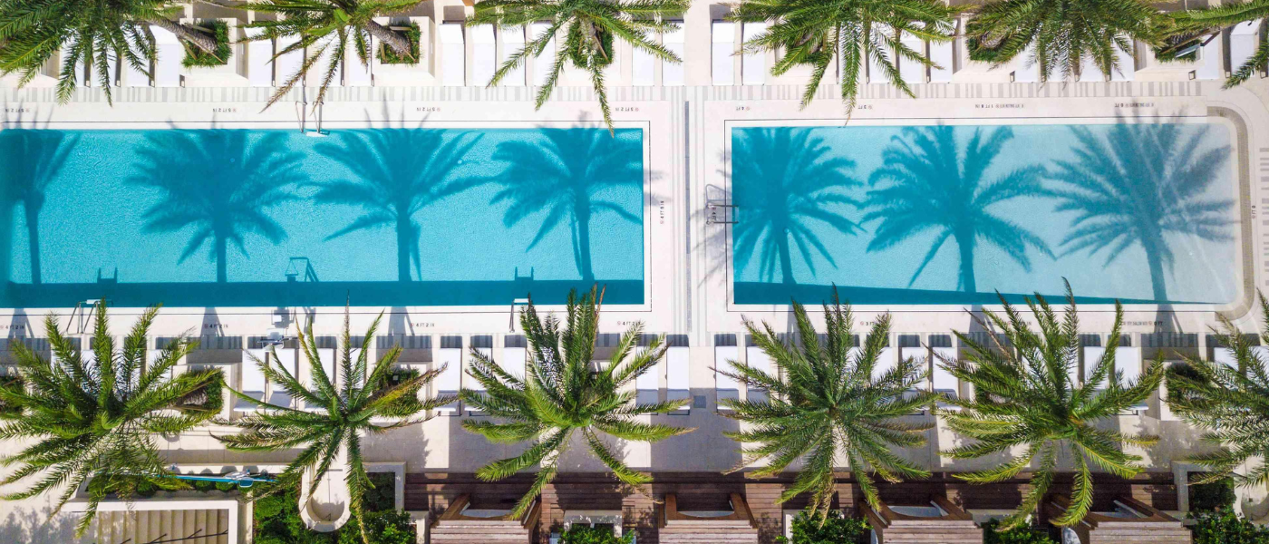 an aerial shot of two pools lined with palm trees