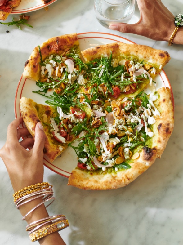 a hand decorated in gold bangles reaching for a piece of pizza