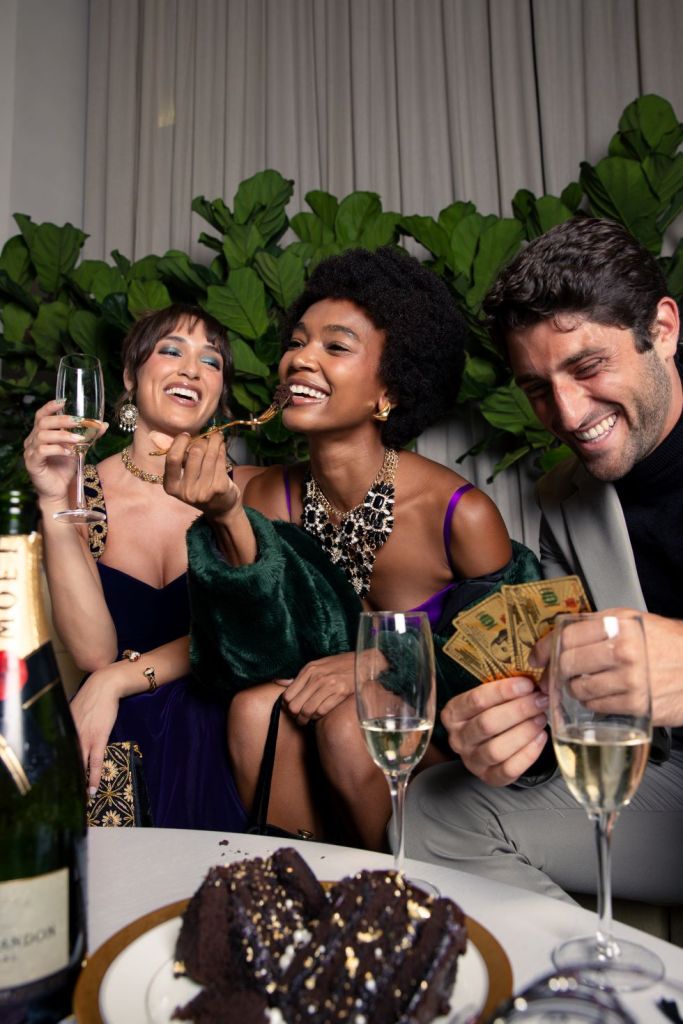 2 female models and 1 male model eat together with champagne and chocolate cake