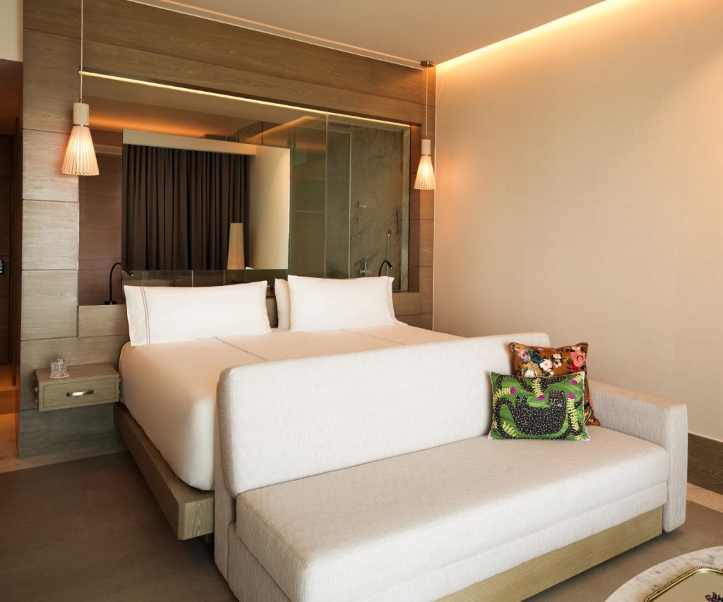 a king bedroom with two hanging scones over the bedside tables and a bench in front with lavish throw pillows