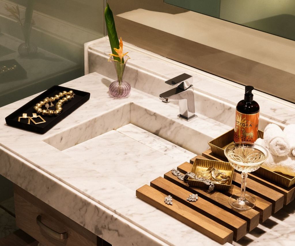 a close up of a marble sinks with jewelry displayed on the counter next to it and a coup glass of champagne.