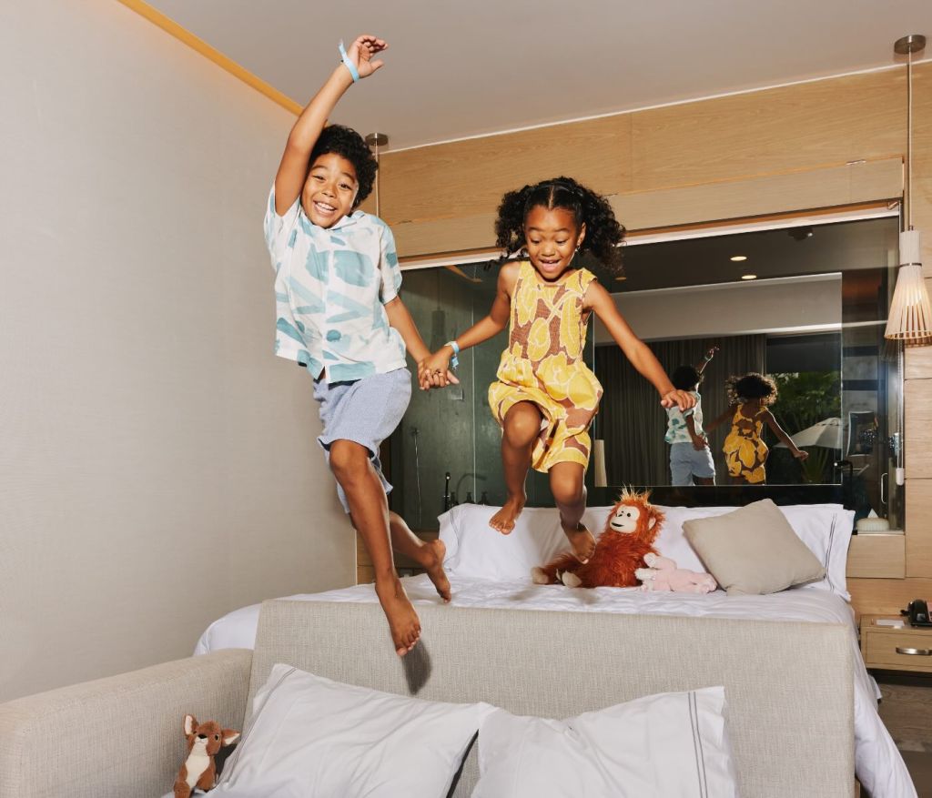 two kids staying at SLS Playa Mujeres, having fun jumping on the bed in their room