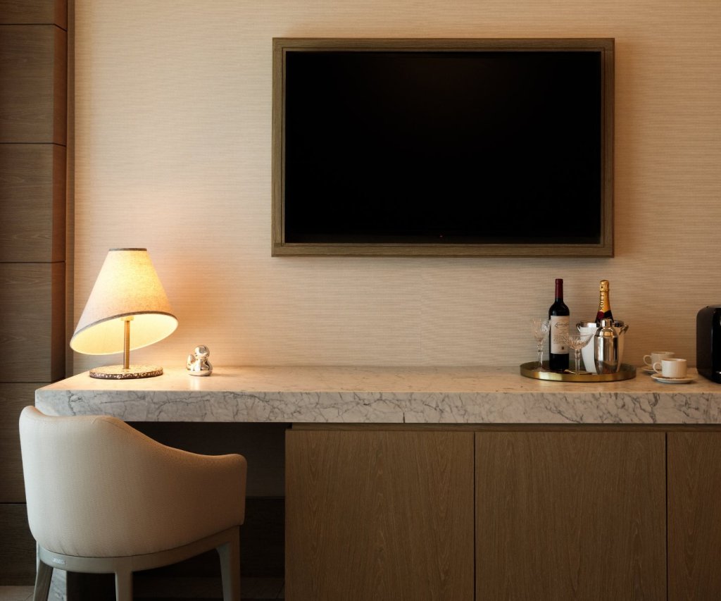 a desk with a whimsical lamp, a platter of wine and glasses, and an HDTV mounted above it on the wall