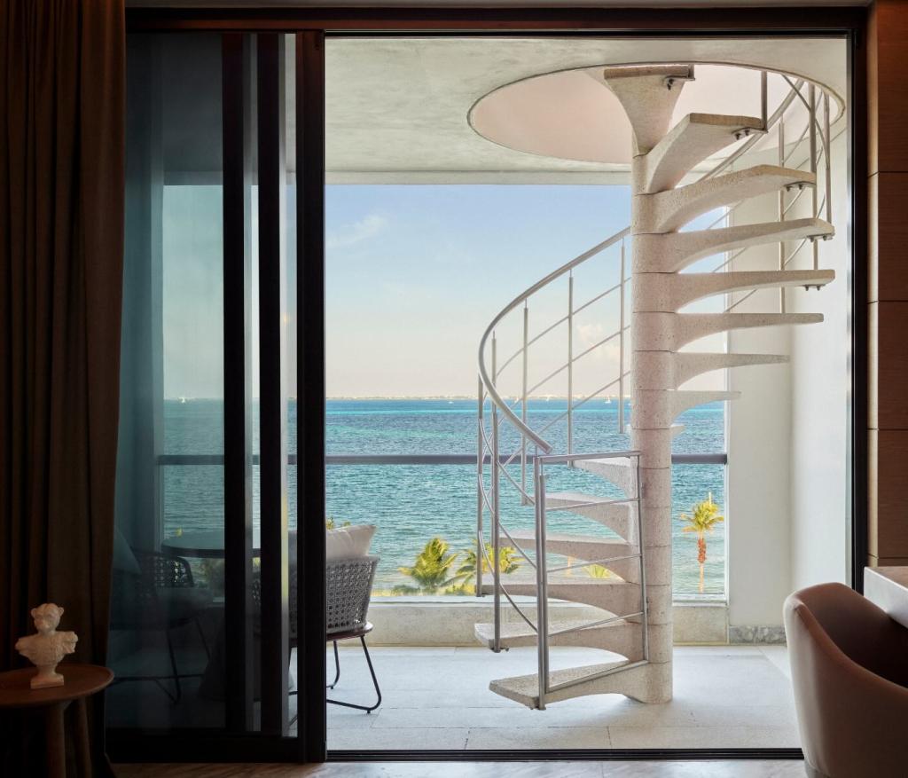 a sliding glass door that is open to a stunning terrace with a spiral staircase overlooking the ocean.