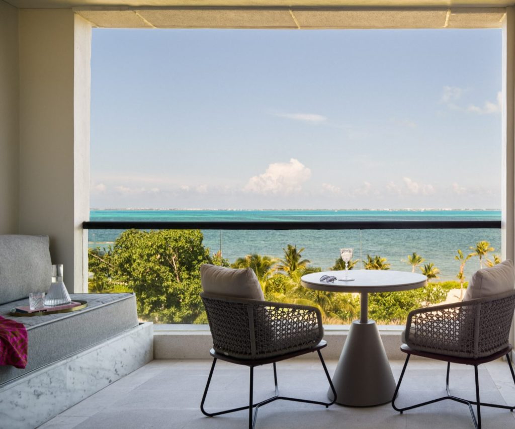 two chairs around a small table with a glass of champagne and sunglasses on top on a terrace overlooking the ocean